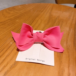 Detailed view of a bright pink fabric bow hair clip on a white display card over wood