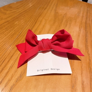 Close-up of bright red fabric bow hair clip with long ribbons on a display card