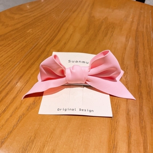 Detailed macro view of a 3D pink candy-colored bow hair clip on a branded white display card
