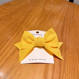 Detail of a bright yellow fabric bow hair clip on a white display card over wood