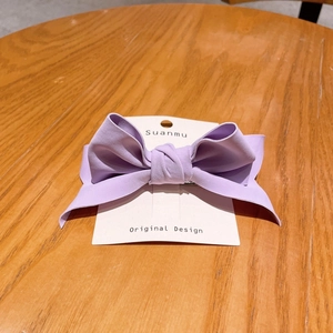Close-up of purple chiffon bow hair clip displayed on an original design white card