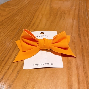 Detailed close-up of a vibrant orange fabric bow hair clip on an original design card
