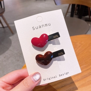 Close-up of heart-shaped hair clips in red and coffee brown with handmade gold lettering