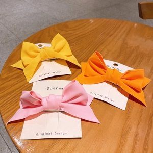 Three colorful fabric bow hair clips in yellow orange and pink on a wooden background