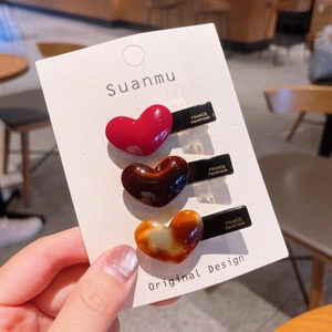 Detailed view of three glossy heart-shaped acetate hair clips with metal alligator grip