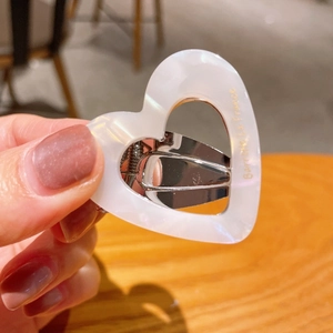 Close-up of white acetate heart hair clip with gold logo held in a hand