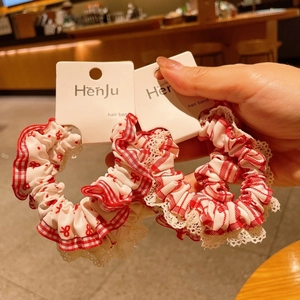 Detail of red gingham scrunchies with white lace edges and bow print held in hand
