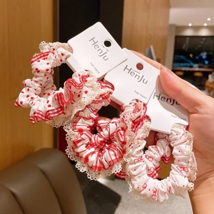 Three red sweet hair scrunchies with white lace edges in plaid and polka dot patterns