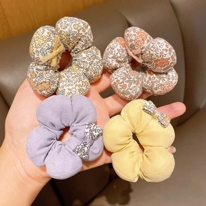 Set of four floral cotton scrunchies with bow details held in hand showing fabric texture