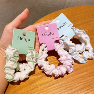 Detail of ruffled floral hair scrunchies in green, blue and purple on wooden surface