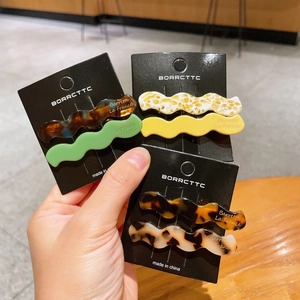 Set of wavy acetate hair clips in tortoiseshell and marble patterns on black card
