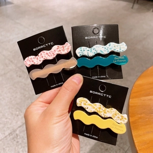 Close-up of wavy acetate hair clips in multiple floral and solid colors on a card