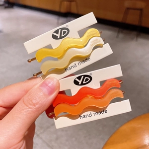 Detail view of wavy acetate hair clips in warm yellow and orange tones with gold metal base