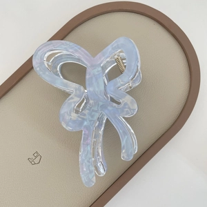 Macro shot of light blue bow hair claw clip with aurora finish on beige leather tray