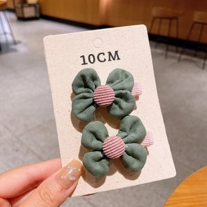 Detailed close-up of green fabric bow hair clips with pink buttons on display card