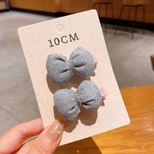 Detail showing two grey handmade bow hair clips with silver thread on a 10cm card