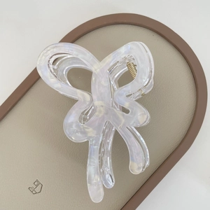 Close-up of translucent iridescent butterfly hair claw clip on a beige textured tray