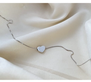 Close-up of minimalist silver heart necklace on elegant white silk fabric texture