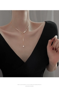 Detail view of a gold Y-shaped tassel necklace with elegant pearls on a female model