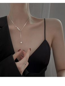 Close-up of a silver Y-shaped pearl necklace on a model highlighting the collarbone