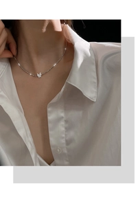 Close-up of a sparkling 925 silver butterfly pendant necklace worn on a satin white shirt