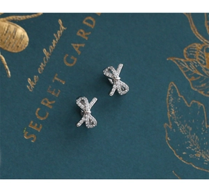 Close-up of elegant bow earrings with pavé zircons on a dark green botanical background