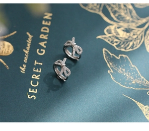 Macro shot of silver bow hoop earrings with micro-set zircons on a dark green book