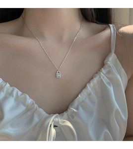 Close-up of sparkling silver lock necklace pendant with square stone on silk dress