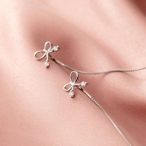 Boucles d'oreilles nœud en argent S925 avec zircones sur fond de satin rose