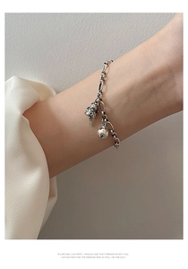 Detail of silver chain bracelet with vintage bell charm and smooth bead on female wrist