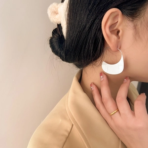 Detail of trendy silver large crescent metal earrings with mirror finish on female model