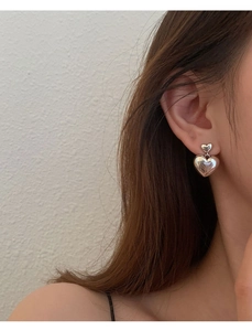 Gros plan de boucles d'oreilles cœur en argent S925 poli portées par un mannequin élégant