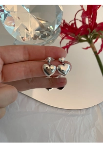 Gros plan de boucles d'oreilles en argent 925 poli en forme de cœur tenues à la main