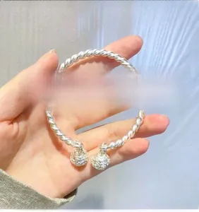 Detailed close-up of a twisted silver-tone bangle featuring two hollow bell charms being held