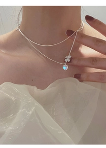 Double-layered silver necklace with heart pendant and flower detail on female neck