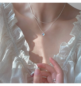 Detail of double-layered silver heart pendant necklace with moonstone on woman collarbone