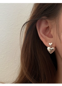 Gros plan de boucles d'oreilles doubles cœurs en argent s925 poli portées sur l'oreille