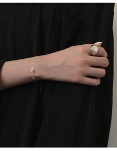 Close-up of minimalist silver pearl bracelet and engraved signet ring on skin