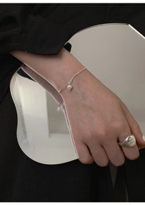 Minimalist pearl bracelet and hammered metal ring shown via artistic mirror reflection