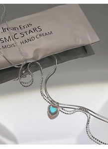 Macro shot of 925 silver heart necklace with blue-green gem and dual layered chain
