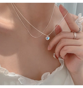 Close-up of heart pendant necklace with iridescent blue stone and layered silver chains
