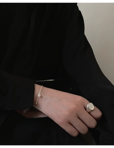 Close-up of minimalist silver pearl bracelet and engraved metal seal ring worn by model