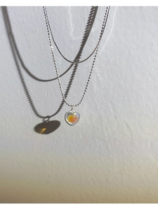 Detail of a layered silver heart pendant necklace with iridescent opal on stone wall