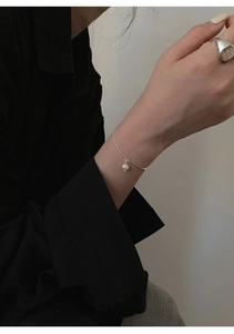 Detailed view of a minimalist pearl bracelet and wide silver ring worn by a model