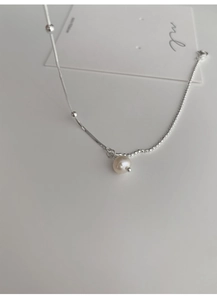 Detail shot of a minimalist silver chain necklace featuring a single white pearl pendant