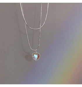 Close-up of double-layer silver heart necklace featuring a shiny opal pendant and snake chain