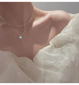 Close-up of double-layered 925 silver necklace with heart pendant on elegant female model
