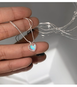 Close-up of heart-shaped opal pendant on a silver ball chain necklace showing rainbow effect