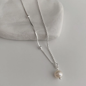Minimalist double-layer silver chain necklace with a natural white pearl pendant on stone