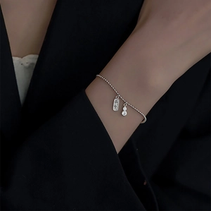 Détail du bracelet à perles argentées avec pampille gravée et pendentif gourde